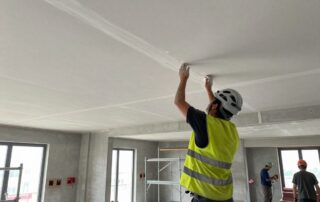 Stukkateur trägt Helm und Reflektionsweste, während er dekorativen Putz an einer hohen Decke aufträgt