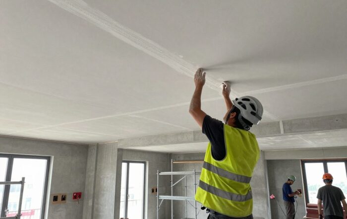 Stukkateur trägt Helm und Reflektionsweste, während er dekorativen Putz an einer hohen Decke aufträgt