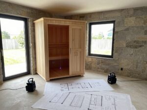 Weitwinkelaufnahme eines modernen deutschen Innenraums mit teilweise gebauter Sauna-Kabinett, detaillierten Grundrissen und Laserscanning-Ausrüstung auf dem Boden