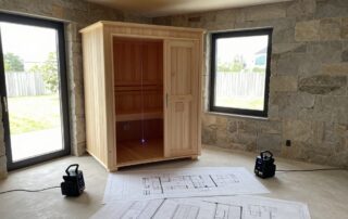 Weitwinkelaufnahme eines modernen deutschen Innenraums mit teilweise gebauter Sauna-Kabinett, detaillierten Grundrissen und Laserscanning-Ausrüstung auf dem Boden