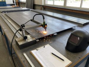 Plasma-Schneider schneidet Stahlblech in einer sauberen deutschen Schweißwerkstatt mit Messwerkzeugen und Sicherheitsausrüstung