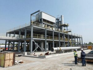 Weitwinkelaufnahme eines modernen deutschen Industrieanlagens bei Bau, Stahlrahmen, Betonfundament und großen Rohren, Arbeiter mit Helmen prüfen den Standort