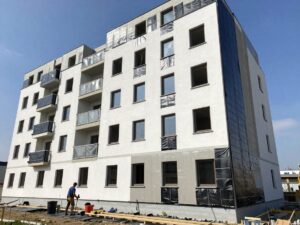 Moderne deutsche Wohngebäude mit teilweise fertiggestellter Außenwand, sichtbaren Abdichtungs‑Schichten und Arbeitern, die Bitumenmembranen verlegen