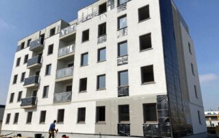 Moderne deutsche Wohngebäude mit teilweise fertiggestellter Außenwand, sichtbaren Abdichtungs‑Schichten und Arbeitern, die Bitumenmembranen verlegen