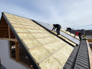 Arbeiter installieren Dämmplatten auf einem schrägen deutschen Wohnhausdach unter klarem Himmel