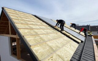 Arbeiter installieren Dämmplatten auf einem schrägen deutschen Wohnhausdach unter klarem Himmel