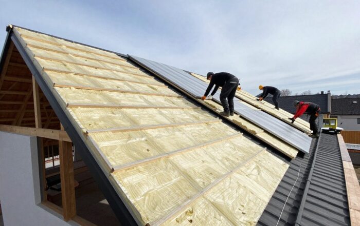 Arbeiter installieren Dämmplatten auf einem schrägen deutschen Wohnhausdach unter klarem Himmel