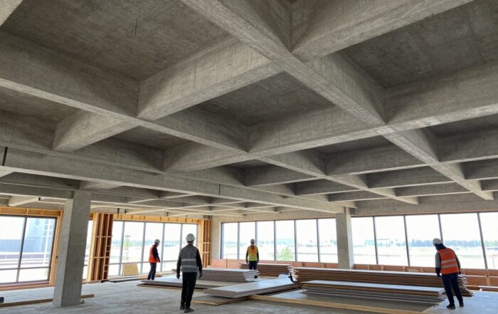 Modernes Baustellenbild mit teilweise fertiggestellter Decke aus Betonbalken, Holzbalken und Gipskartonplatten, Arbeiter tragen Helme und Warnwesten