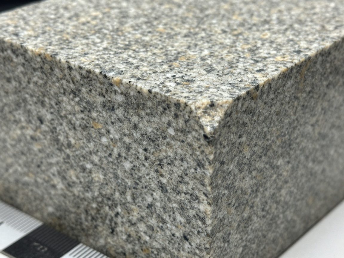 Makroaufnahme eines Granitblocks mit sichtbarem Kornmuster, Maßstab durch Lineal, leichte Schatten und Staubwolke für Realismus