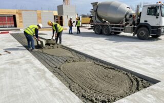 Arbeiter mit Helmen und Warnwesten mischen Zementestrich auf einer neuen Betonplatte bei Tageslicht