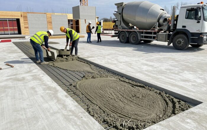 Arbeiter mit Helmen und Warnwesten mischen Zementestrich auf einer neuen Betonplatte bei Tageslicht