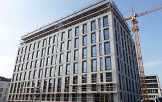 Weitwinkelaufnahme einer modernen deutschen Bürogebäudefassade im Bau: Gerüst, Arbeiter in Sicherheitswesten verlegen Klappentafeln, Kran im Hintergrund