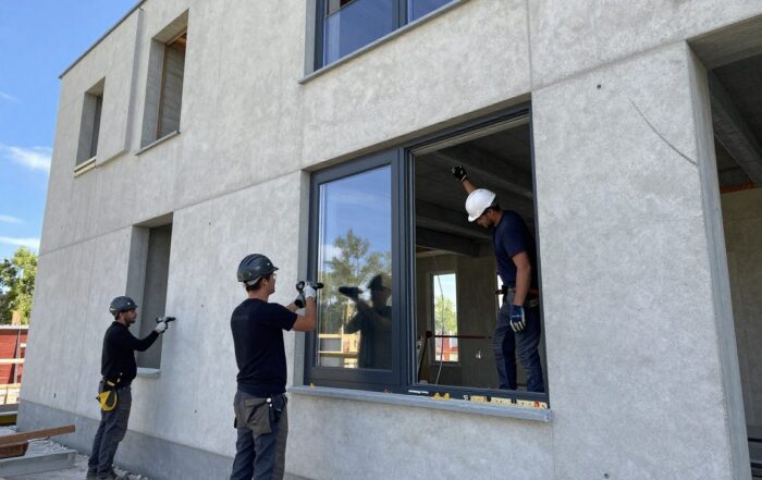 Arbeiter installieren Doppelverglasung an einer Wohnhausfassade auf einem modernen deutschen Baustellenplatz bei Tageslicht