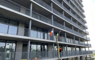 Weitwinkelaufnahme eines modernen Stahlgeländers in der Konstruktion an einem deutschen Hochhaus, Arbeiter schweißen und messen bei hellem Tageslicht