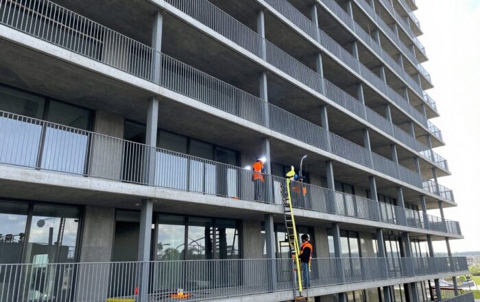 Weitwinkelaufnahme eines modernen Stahlgeländers in der Konstruktion an einem deutschen Hochhaus, Arbeiter schweißen und messen bei hellem Tageslicht