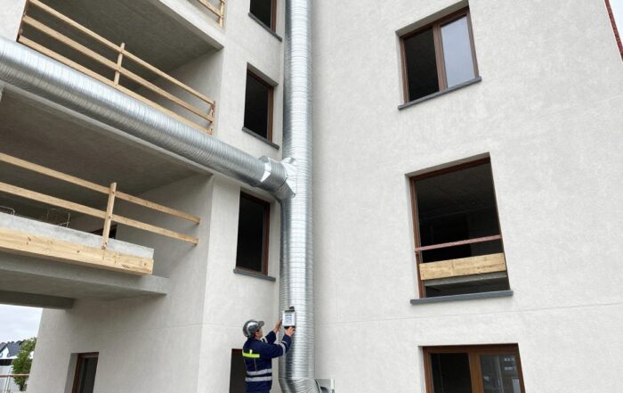 Techniker misst Temperaturen an moderner deutschen Wohngebäude mit sichtbarem HVAC-Rohrwerk