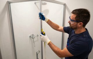 Professioneller Klempner legt eine schlichte, rahmenlose Duschkabine in einem deutschen Badezimmer an, trägt Schutzbrille und Handschuhe