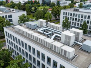 Weitwinkelaufnahme eines modernen deutschen Bürogebäudes mit integrierten HLK-Anlagen auf dem Dach und sichtbaren Rohrleitungen, umgeben von üppigem Grün
