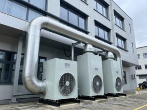 Breitwinkelaufnahme einer modernen Gewerbebau-Lüftungsanlage mit Rohrleitungen, Ventilatoren und Wärmetauschern, die in das Fassadendesign integriert sind