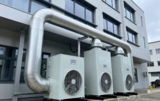 Breitwinkelaufnahme einer modernen Gewerbebau-Lüftungsanlage mit Rohrleitungen, Ventilatoren und Wärmetauschern, die in das Fassadendesign integriert sind