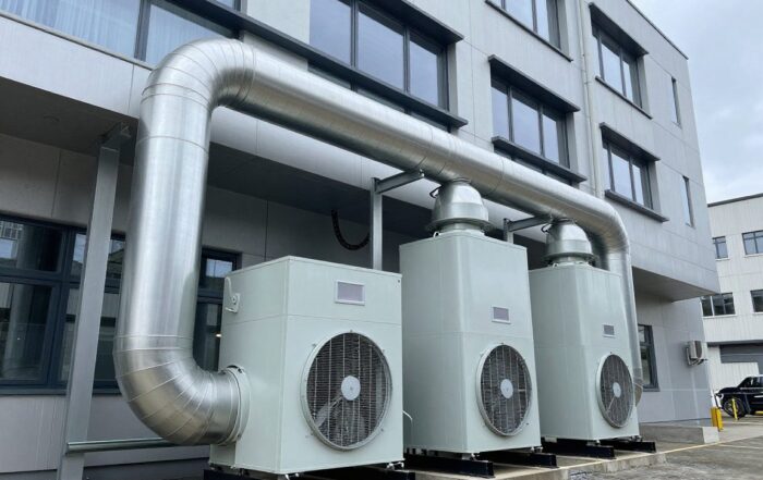 Breitwinkelaufnahme einer modernen Gewerbebau-Lüftungsanlage mit Rohrleitungen, Ventilatoren und Wärmetauschern, die in das Fassadendesign integriert sind