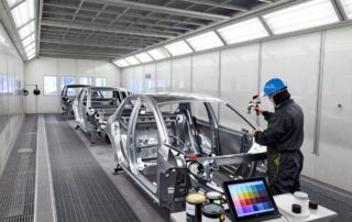 Techniker in Schutzkleidung sprüht Farbe auf Metallrahmen in einer modernen deutschen Lackierhalle