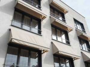 Weitwinkelaufnahme eines modernen deutschen Wohnhauses mit ausfahrbaren Markisen an den Fenstern, sichtbare Stoffstruktur und Metallrahmen im Sonnenlicht