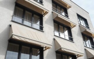 Weitwinkelaufnahme eines modernen deutschen Wohnhauses mit ausfahrbaren Markisen an den Fenstern, sichtbare Stoffstruktur und Metallrahmen im Sonnenlicht