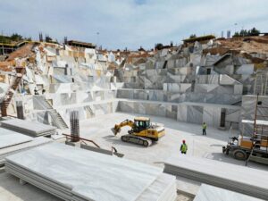 Weitwinkelaufnahme einer deutschen Baustelle mit großen Marmorförderanlagen, schweren Maschinen und Arbeitern in Schutzkleidung, umgeben von teilweise fertigen Marmorschalen