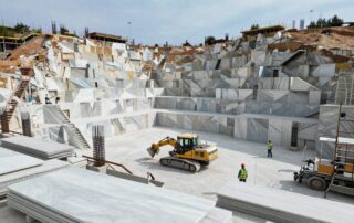 Weitwinkelaufnahme einer deutschen Baustelle mit großen Marmorförderanlagen, schweren Maschinen und Arbeitern in Schutzkleidung, umgeben von teilweise fertigen Marmorschalen