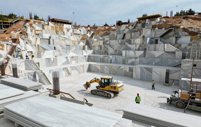 Weitwinkelaufnahme einer deutschen Baustelle mit großen Marmorförderanlagen, schweren Maschinen und Arbeitern in Schutzkleidung, umgeben von teilweise fertigen Marmorschalen