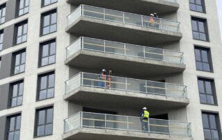 Weitwinkelaufnahme eines modernen deutschen Wohngebäudes mit neuem Balkon im Aufbau – Stahlrahmen, Betonplatten, Arbeiter in Schutzkleidung messen Dimensionen