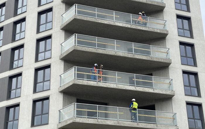 Weitwinkelaufnahme eines modernen deutschen Wohngebäudes mit neuem Balkon im Aufbau – Stahlrahmen, Betonplatten, Arbeiter in Schutzkleidung messen Dimensionen