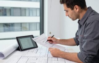 Ein deutscher Bausanierer prüft digitale Schadensberichte und zeichnet ein Protokoll auf einem Tablet, während Wasserflecken an einer Gebäudewand sichtbar sind.