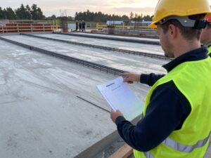 Baustellenvorarbeiter mit Biegeliste und Ablaufliste auf einer frisch gegossenen Betonplatte, umgeben von Stahlbetonstäben