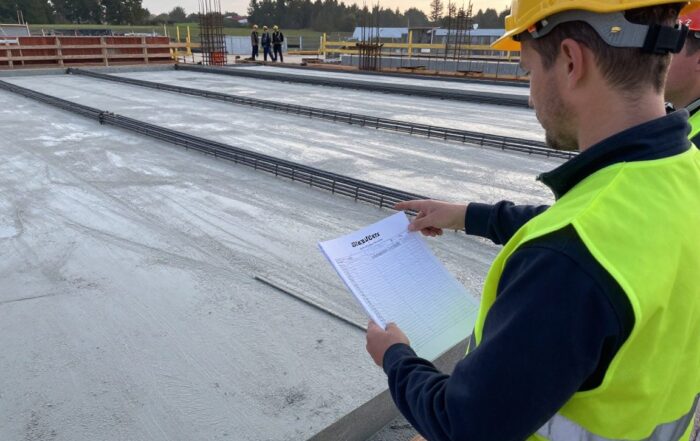Baustellenvorarbeiter mit Biegeliste und Ablaufliste auf einer frisch gegossenen Betonplatte, umgeben von Stahlbetonstäben