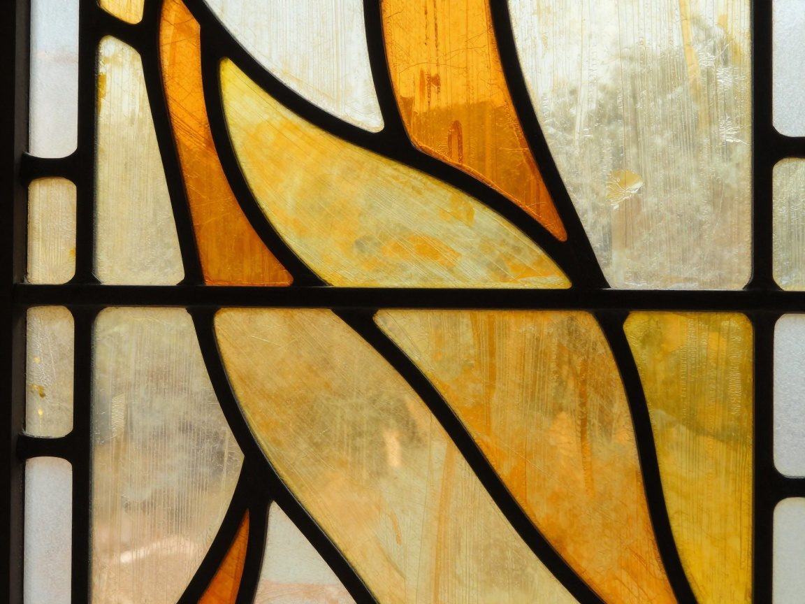 Nahaufnahme eines Bleiglasfensters: warme Gelb- und Orangetöne in fließendem Muster, betonte Bleileitungen, sanftes Tageslicht erzeugt Wärme und leichte Reflexionen
