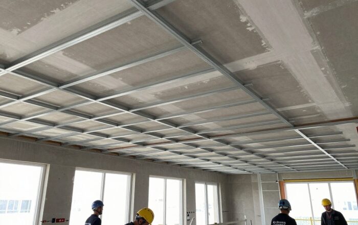 Blick auf Baustelle: teilweise fertige Decke mit Stahlrahmen und Gipskartonplatten, Arbeiter messen mit Laserschnellgerät