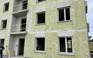 Weitwinkelaufnahme eines deutschen Wohngebäudes in der Baustelle mit freiliegenden Wänden, Dämmplatten aus Steinwolle und XPS sowie Arbeitern, die Maßband und Lasermessgerät benutzen