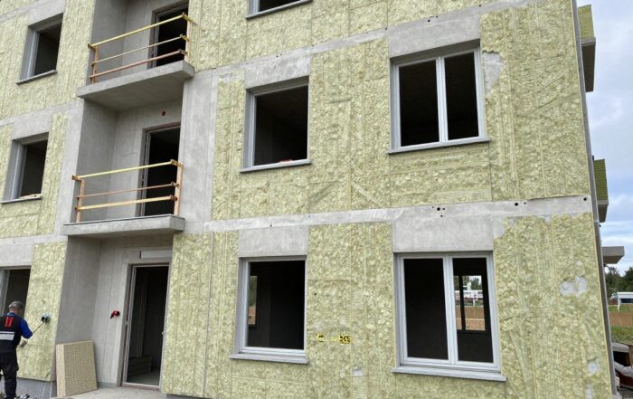 Weitwinkelaufnahme eines deutschen Wohngebäudes in der Baustelle mit freiliegenden Wänden, Dämmplatten aus Steinwolle und XPS sowie Arbeitern, die Maßband und Lasermessgerät benutzen