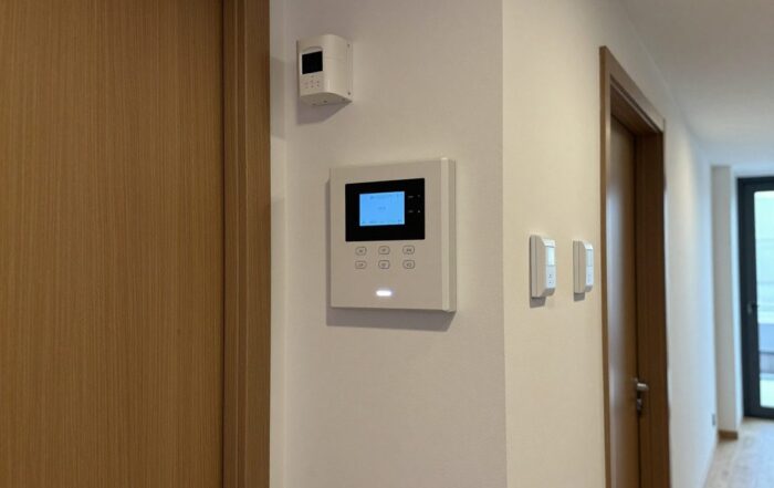 Wandmontierte Steuerzentrale mit digitalem Display, Bewegungsmelder und Türkontakt an einer deutschen Wohnhall