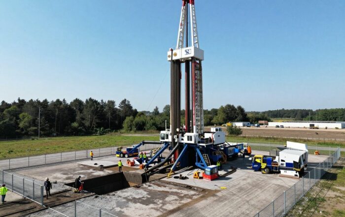 Große Diesel-Bohrmaschine auf kompakter Kiesfläche mit ausfahrbarem Arm über einem gebohrten Loch, umgeben von Sicherheitszaun und klarer Himmel