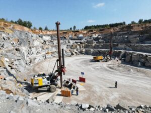 Großaufnahme eines deutschen Steinbruchs bei Tageslicht mit Bohrgeräten, Sicherheitsbarrieren und Arbeitern in Helmen