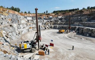 Großaufnahme eines deutschen Steinbruchs bei Tageslicht mit Bohrgeräten, Sicherheitsbarrieren und Arbeitern in Helmen