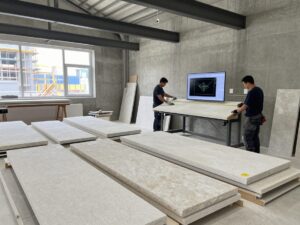 Weitwinkelaufnahme eines deutschen Steinmetzbetriebs mit CAD-Software auf einem Tisch, Steinplatten und Handwerkern in Arbeitsglehn