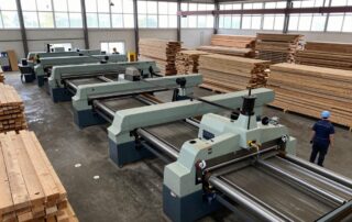 Weitwinkelaufnahme eines modernen deutschen Sägewerks mit Reihen von Sägemaschinen, Holzstapeln und Arbeitern in Schutzhelmen unter natürlichem Licht