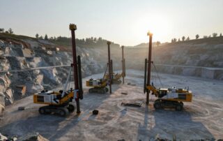 Weitwinkelaufnahme eines deutschen Steinbruchs bei Sonnenaufgang, mit Reihen großer Bohrmaschinen und schwerer Ausrüstung auf rauem Felsbett