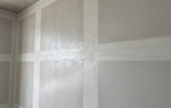 Nahaufnahme einer deutschen Baustelle mit Trockenbauwand, sauber gefüllten Fugen und abgedeckten Schraubenköpfen, glatt polierter Beton