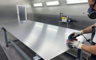 Arbeiter schneidet mit 120‑Körnungsschleifblock ein Metallblech in einer modernen Lackierwerkstatt, um die Oberfläche für den Anstrich vorzubereiten
