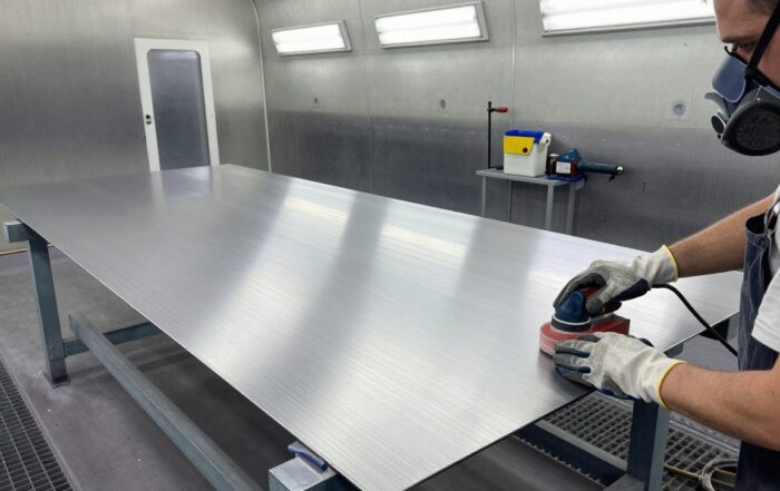 Arbeiter schneidet mit 120‑Körnungsschleifblock ein Metallblech in einer modernen Lackierwerkstatt, um die Oberfläche für den Anstrich vorzubereiten